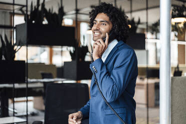 Lächelnder männlicher Berufstätiger im Gespräch am Festnetztelefon im Büro - JOSEF02842