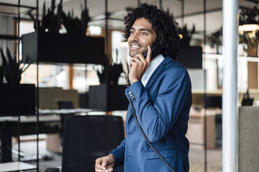 Smiling male professional talking on landline phone in office - JOSEF02842