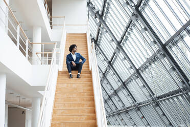 Thoughtful businessman sitting on staircase while looking away - JOSEF02847