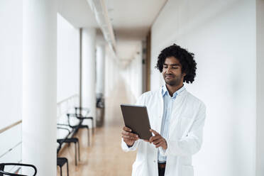 Selbstbewusster junger Arzt mit digitalem Tablet auf dem Krankenhausflur - JOSEF02850