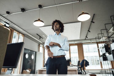 Confident young male professional rolling up sleeves in office - JOSEF02876