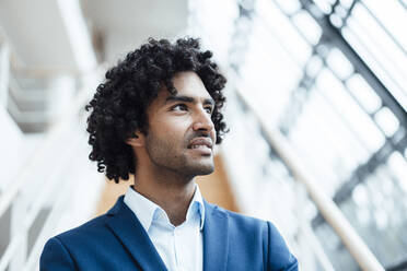Thoughtful businessman with curly black hair looking away at office - JOSEF02894