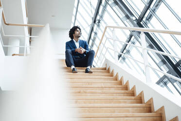 Nachdenklicher männlicher Fachmann, der auf einer Treppe sitzt und im Büro wegschaut - JOSEF02895