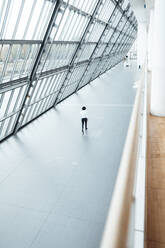 Young male professional walking in corridor by roof at office - JOSEF02908