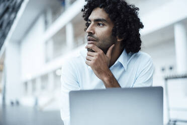 Thoughtful young businessman with hand on chin looking away at office - JOSEF02913