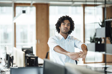 Young male entrepreneur stretching while looking away in office - JOSEF02945