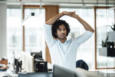 Young businessman stretching with arms raised while looking away in office - JOSEF02946