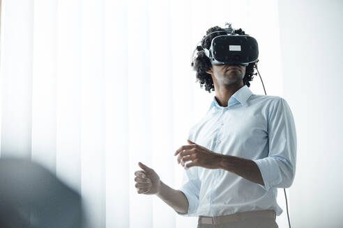 Junger männlicher Unternehmer trägt ein Virtual-Reality-Headset im Sitzungssaal seines Büros - JOSEF02948