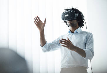 Junger Geschäftsmann trägt ein Virtual-Reality-Headset, während er im Sitzungssaal im Büro gestikuliert - JOSEF02949