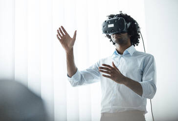 Young businessman wearing virtual reality headset while gesturing in board room at office - JOSEF02949