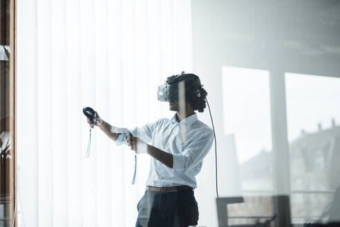 Young male entrepreneur wearing virtual reality headset playing with joystick in board room at office - JOSEF02951