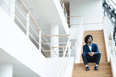 Nachdenklicher männlicher Berufstätiger, der auf einer Treppe im Büro sitzt und wegschaut - JOSEF02962