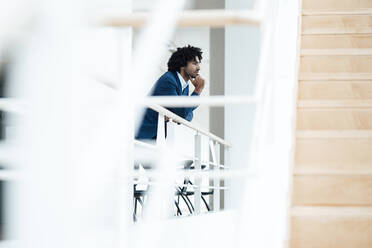 Thoughtful businessman leaning on railing by staircase in office - JOSEF02964