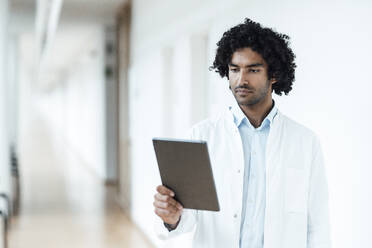 Selbstbewusster junger Arzt mit digitalem Tablet auf dem Flur eines Krankenhauses - JOSEF02972