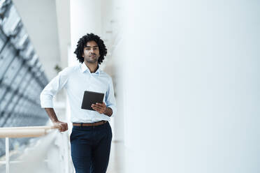 Selbstbewusster Geschäftsmann, der ein digitales Tablet in der Hand hält, während er an einem Geländer im Korridor eines Büros steht - JOSEF02979