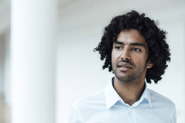 Thoughtful young male entrepreneur with curly black hair looking away at office - JOSEF02984