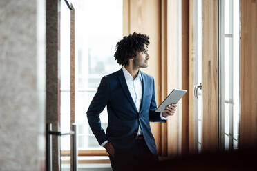 Nachdenklicher männlicher Unternehmer, der ein digitales Tablet in der Hand hält, während er am Arbeitsplatz wegschaut - JOSEF03008