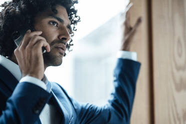 Junger männlicher Berufstätiger, der im Büro mit seinem Handy telefoniert - JOSEF03013