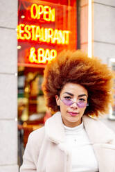 Beautiful woman with afro hair wearing sunglasses while standing against restaurant - OCMF01961