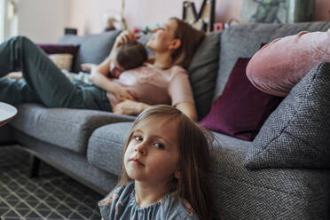 Mutter mit älterer Tochter, während die Schwester unter der Couch im Wohnzimmer sitzt - OGF00740