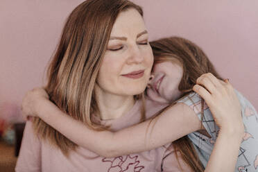 Daughter embracing mother against wall at home - OGF00742