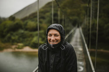 Lächelnde Frau auf der Hängebrücke über den Fluss Sella an einem regnerischen Tag - DMGF00419