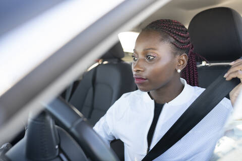 Young woman fastening seat belt while sitting in car stock photo