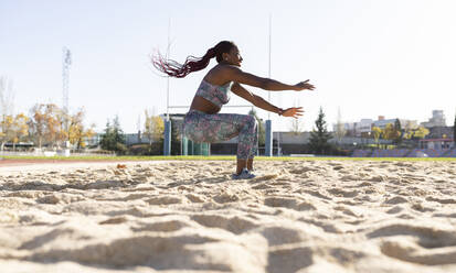 Female sportsperson balancing on sand against clear sky during sunny day - JCCMF00543