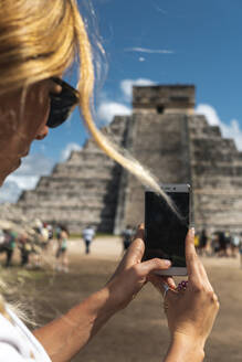 Mexiko, Yucatan, Chichen Itza, Hände eines weiblichen Touristen, der Smartphone-Fotos vom Tempel des Kukulcan macht - JMPF00767