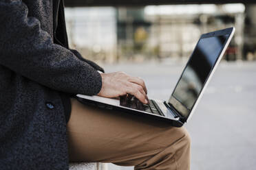 Geschäftsmann, der im Freien sitzend am Laptop arbeitet - EBBF01998