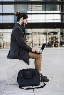 Junger Unternehmer mit Laptop auf einer Bank sitzend - EBBF02000