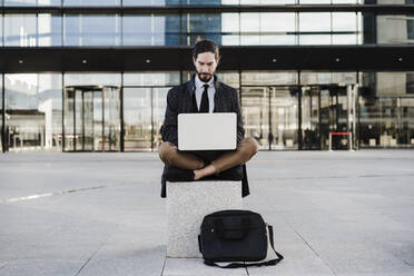 Entrepreneur working on laptop while sitting cross-legged on bench - EBBF02001