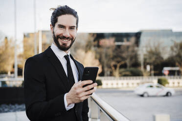 Geschäftsmann lächelnd bei der Verwendung eines Mobiltelefons in der Stadt stehend - EBBF02008