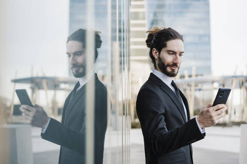 Young entrepreneur using mobile phone while standing by glass wall stock photo