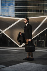 Geschäftsmann mit Jacke, der eine Aktentasche trägt, während er auf einem Fußweg steht - EBBF02017
