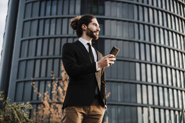 Unternehmer, der ein Mobiltelefon benutzt, während er an einem Gebäude steht - EBBF02020