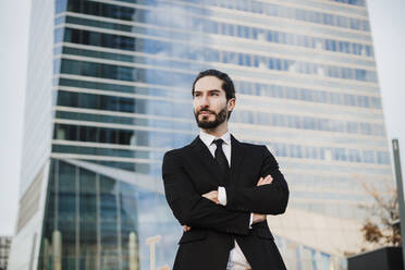 Male entrepreneur with arms crossed looking away while standing in city - EBBF02025