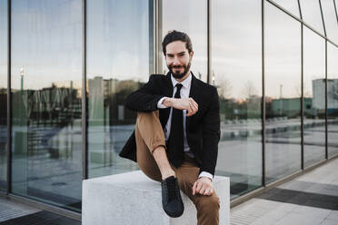 Businessman smiling while sitting on bench against building exterior - EBBF02038