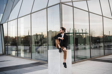 Unternehmer schaut weg, während er an einem Gebäude sitzt - EBBF02042