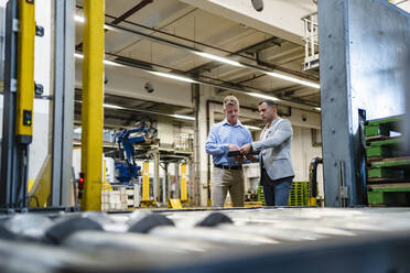 Male entrepreneur with coworker looking at document while working in factory - DIGF14012