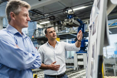 Mature male professional having meeting by whiteboard in factory - DIGF14013