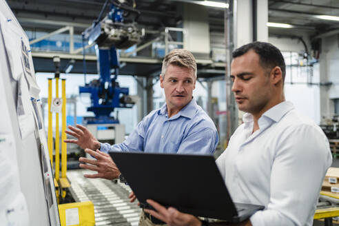Männlicher Vorgesetzter schaut Manager an, während er in einer Besprechung in einer Fabrik einen Laptop benutzt - DIGF14017
