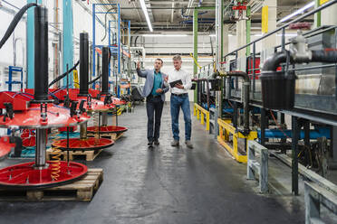 Männliche Kollegen mit digitalem Tablet diskutieren über die Herstellung, während sie in der Fabrik spazieren gehen - DIGF14019