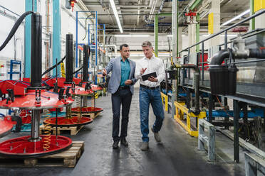 Mature businessman with male colleague discussing over digital tablet while walking in industry - DIGF14020