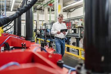 Älterer Manager bei der Arbeit mit einem digitalen Tablet in einer Fabrik - DIGF14025