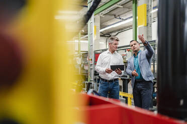 Male engineer explaining male professional about machinery while working in factory - DIGF14026