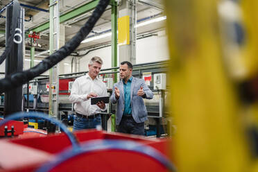 Männlicher Ingenieur und Vorgesetzter arbeiten gemeinsam an einem digitalen Tablet in einer Fabrik - DIGF14027