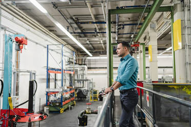 Mature supervisor overlooking machinery while standing in factory - DIGF14034