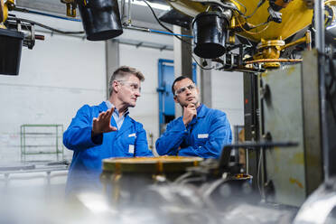 Male technicians wearing protective eyewear discussing on machinery equipment in factory - DIGF14068