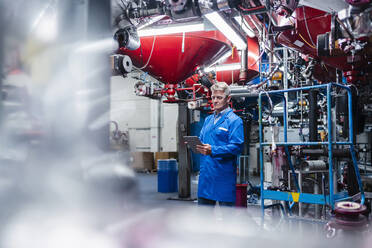 Männlicher Ingenieur, der an einem digitalen Tablet arbeitet, während er an einer Maschine in einer Fabrik steht - DIGF14073